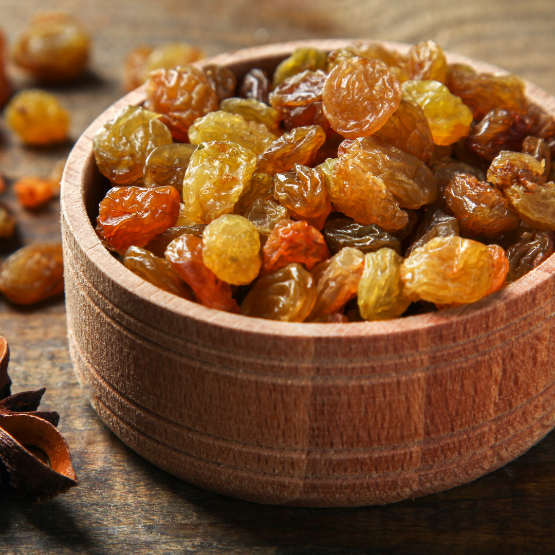 Raisins on a wooden surface surrounded by other dry fruits.